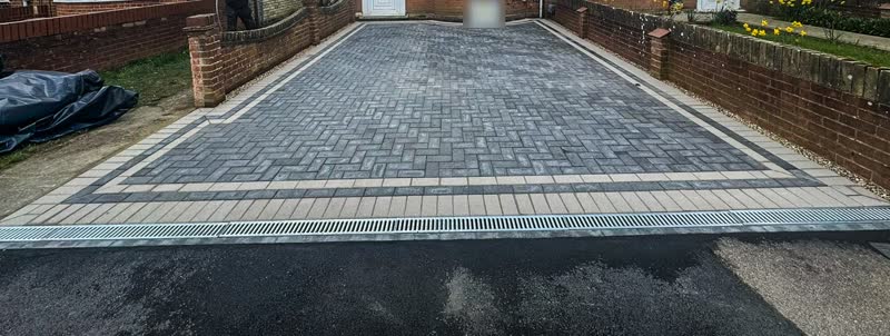 Grey herringbone block paved driveway with a light double border and a channel drain at the pavement edge