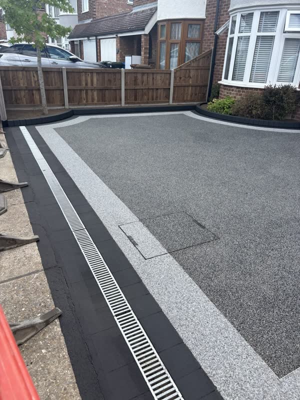 Charcoal resin bound driveway framed by a silver resin border, black block edging and a channel drain along the pavement
