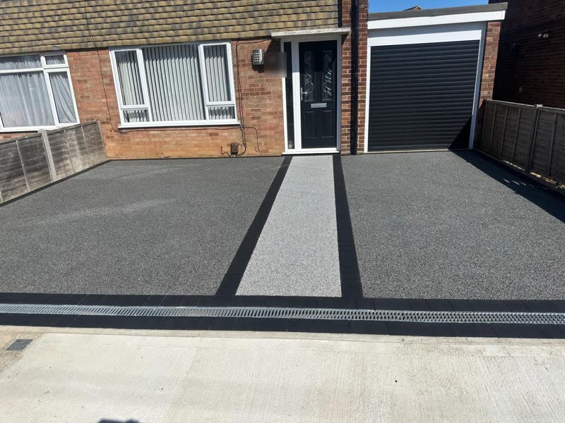 Charcoal resin bound driveway with a lighter silver resin path to the front door, black block edging and a drainage channel