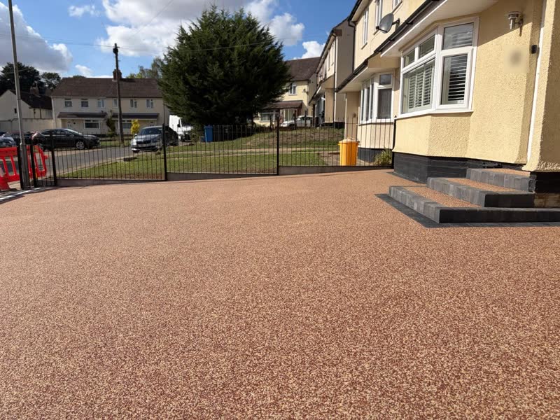 Large red-toned resin bound driveway in front of a semi-detached house, with charcoal block-edged steps up to the front door